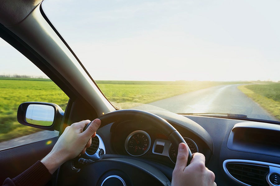 A person driving a car on an open road with the sun shining on the windshield